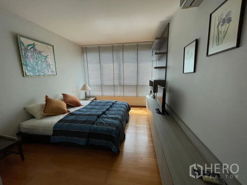 Condominium for sale in Khlong Toei, Bangkok - Spacious bedroom with media wall, shelving and wide window blinds.