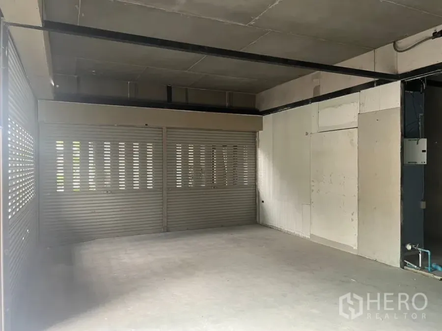 Retail Space for rent in Khlong Toei, Bangkok - Bare-shell retail unit with concrete floor, exposed ceiling and wide perforated roller shutters.