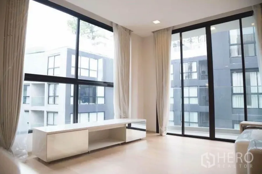 公寓 出租在Watthana, Bangkok - 客厅落地窗与低矮电视柜，俯瞰中庭景观。