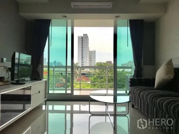 Condominium for rent in Khlong Toei, Bangkok - Bright living room with striped sofa, TV console and a balcony offering city and green views.