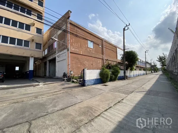 Factory for sale in Bang Phli, Samut Prakan - Entrance driveway next to red-brick factory and wide access road.