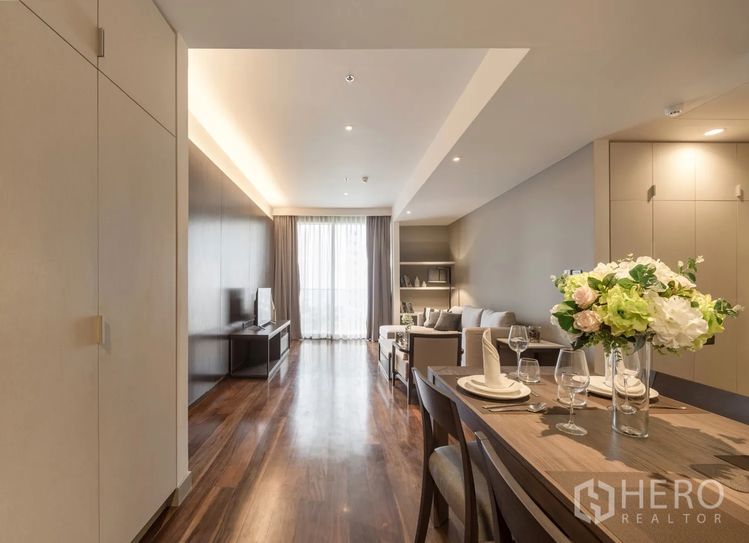 Condominium for rent in Khlong Toei, Bangkok - Open-plan living and dining area with wood floors and a four-seat table with floral centerpiece.
