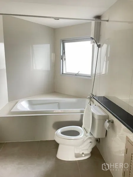 Condominium for rent in Khlong Toei, Bangkok - Clean bathroom with bathtub and shower combo, window, and modern fixtures.