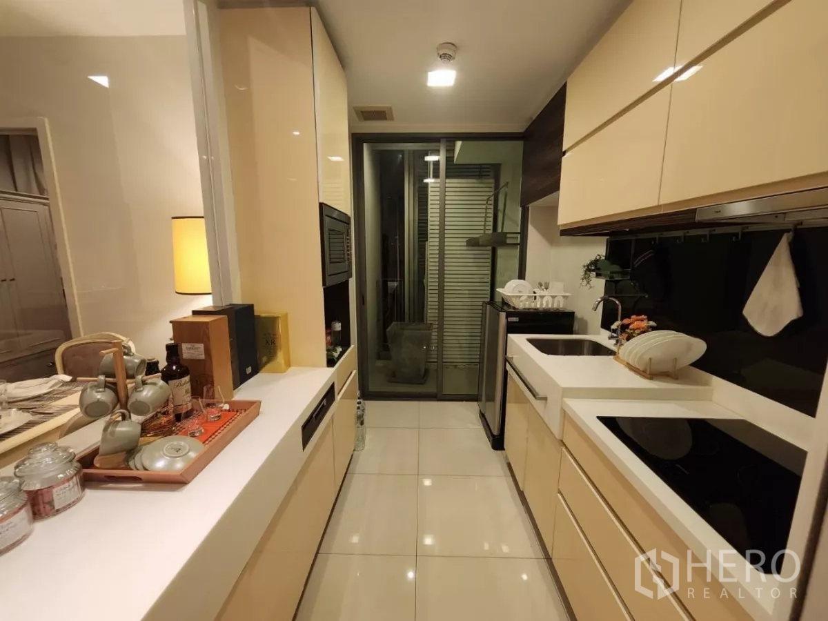 Condominium for rent in Phra Khanong, Bangkok - Galley kitchen with twin countertops leading to a balcony or utility space.