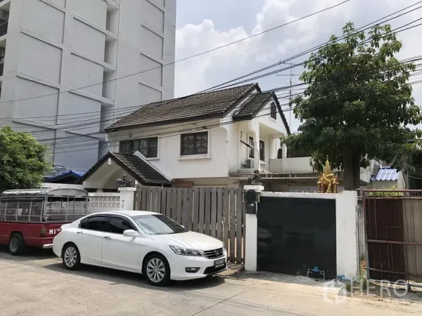 บ้าน ขายในPak Kret, Nonthaburi - ด้านหน้าบ้านเดี่ยวสองชั้นสีขาวพร้อมรั้วไม้ ทางรถเข้าและที่จอดรถ