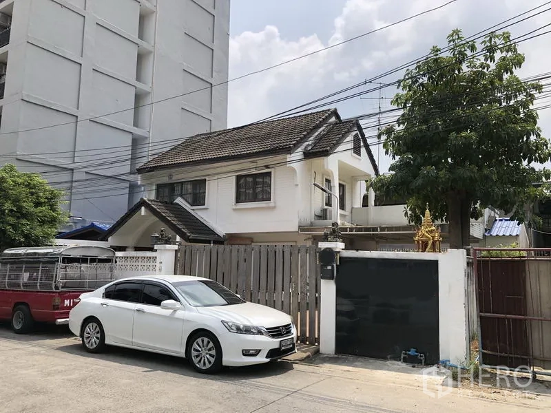 บ้าน ขายในPak Kret, Nonthaburi - ด้านหน้าบ้านเดี่ยวสองชั้นสีขาวพร้อมรั้วไม้ ทางรถเข้าและที่จอดรถ