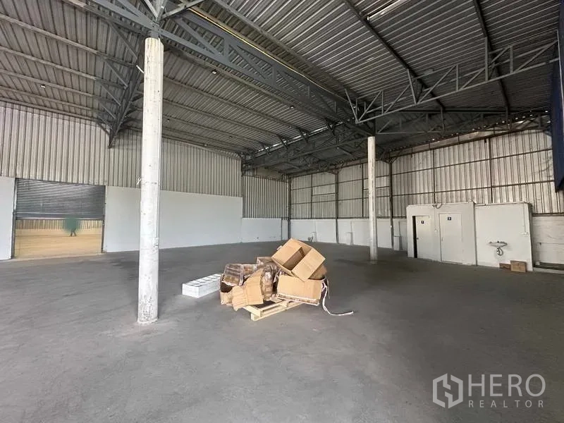 Warehouse for rent in Khlong Luang, Pathum Thani - Warehouse area with roller shutter entry, concrete columns and utility rooms.