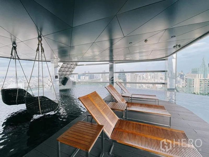 Condominium for rent in Ratchathewi, Bangkok - Rooftop infinity pool deck with loungers and hanging chairs facing the skyline.