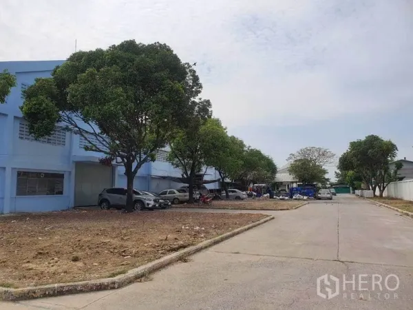 Warehouse for rent in Nakhon Pathom - Access road in the compound with trees and on-site parking beside warehouse blocks.