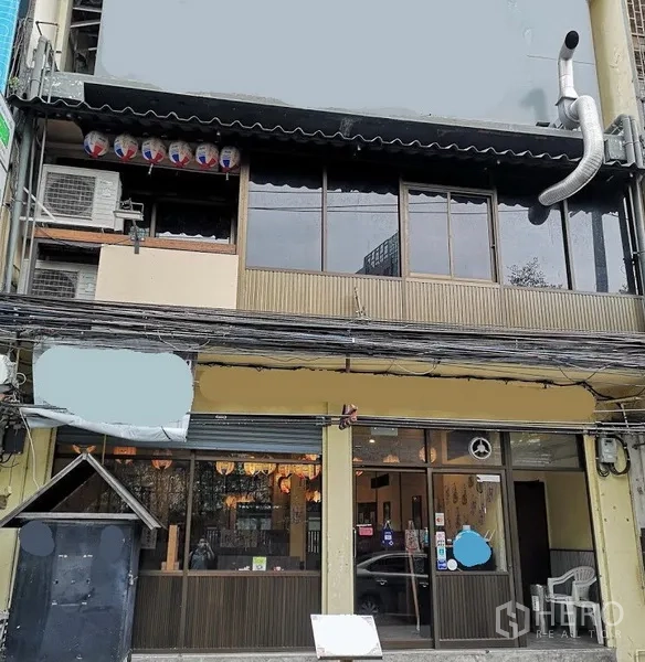 店屋 出租在Watthana, Bangkok - 瓦他那区临街商铺外立面，整面玻璃门面、楼上窗户与厨房排烟管，适合餐饮。