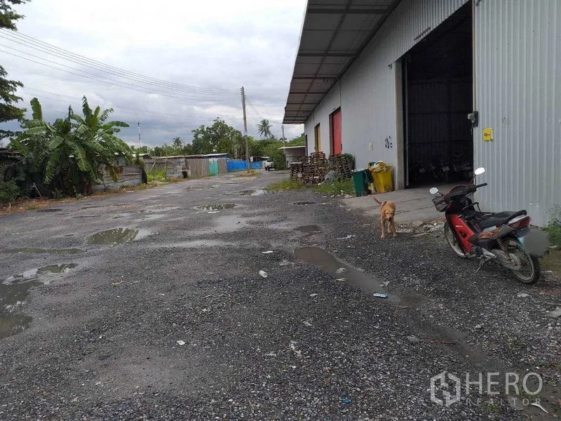 คลังสินค้า ให้เช่าในPak Kret, Nonthaburi - ลานกรวดข้างโกดังผนังเมทัลชีท หลังคายื่นยาว พร้อมประตูม้วนเปิด