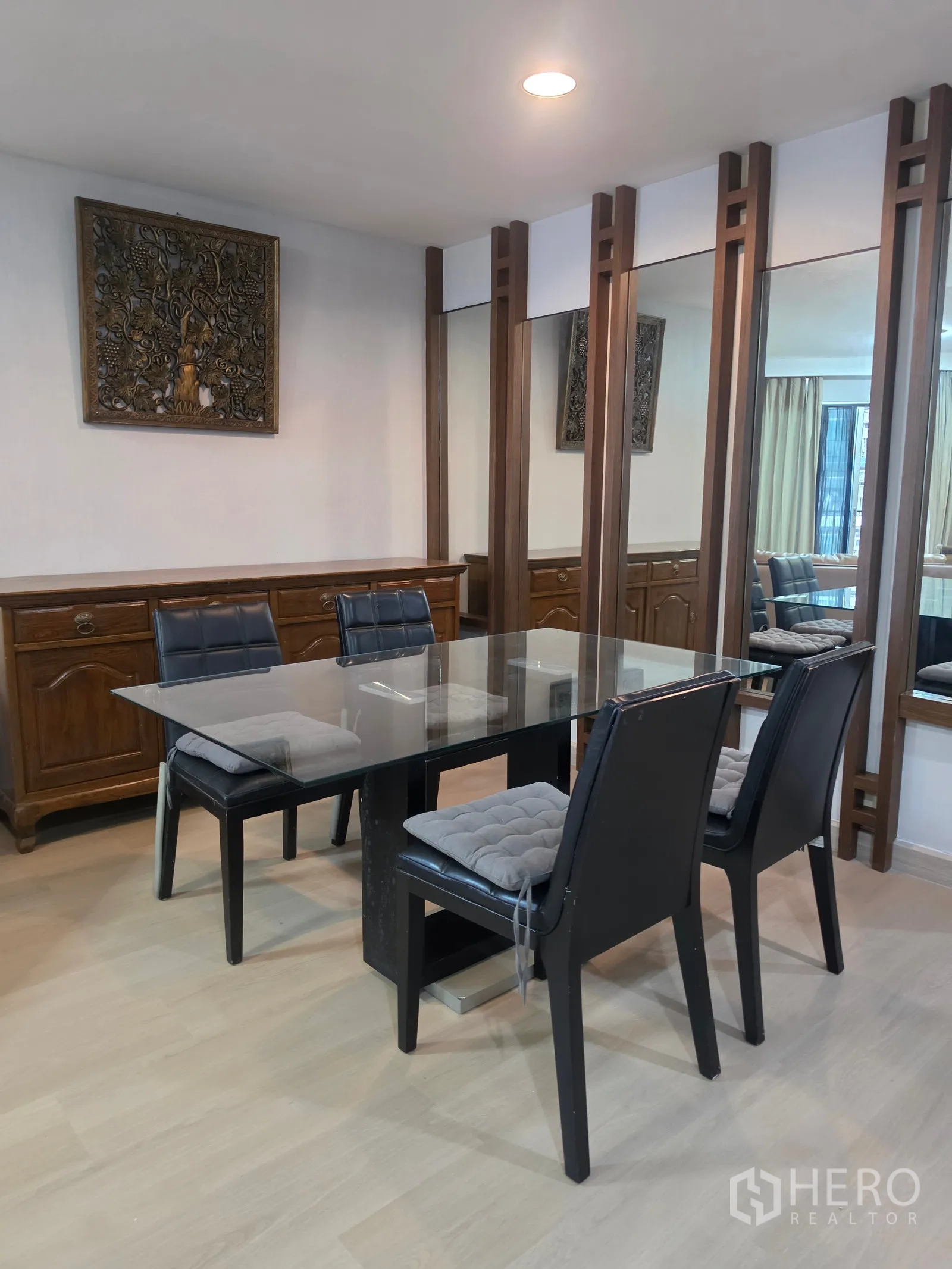 Condominium for rent in Huai Khwang, Bangkok - Dining area with glass-top table, four chairs, wood cabinet, and mirrors.