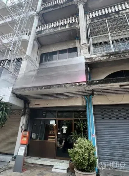 Shophouse for rent in Khlong Toei, Bangkok - Aged multi-storey shophouse facade with sliding glass storefront and balcony details.
