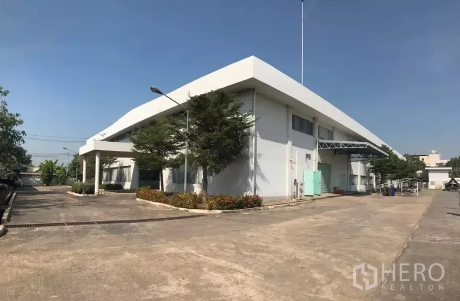 Factory for sale in Khlong Luang, Pathum Thani - Modern white factory exterior with loading bay, wide driveway and landscaping in Khlong Luang.