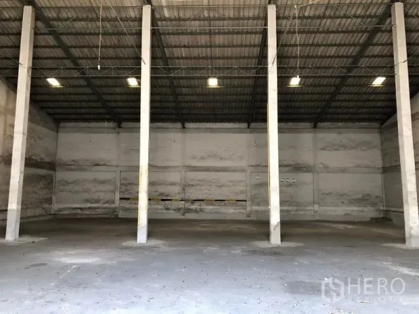 货栈 出租在Lat Krabang, Bangkok - 仓库内部宽敞，高挑屋顶，钢桁架与混凝土地面，中间立柱与顶部照明。