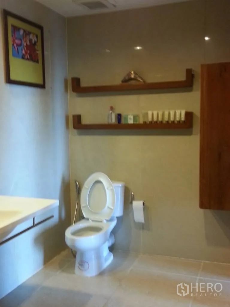 Condominium for rent in Khlong San, Bangkok - Modern bathroom with floating sink, toilet, neutral tiles and wooden wall shelves for toiletries.