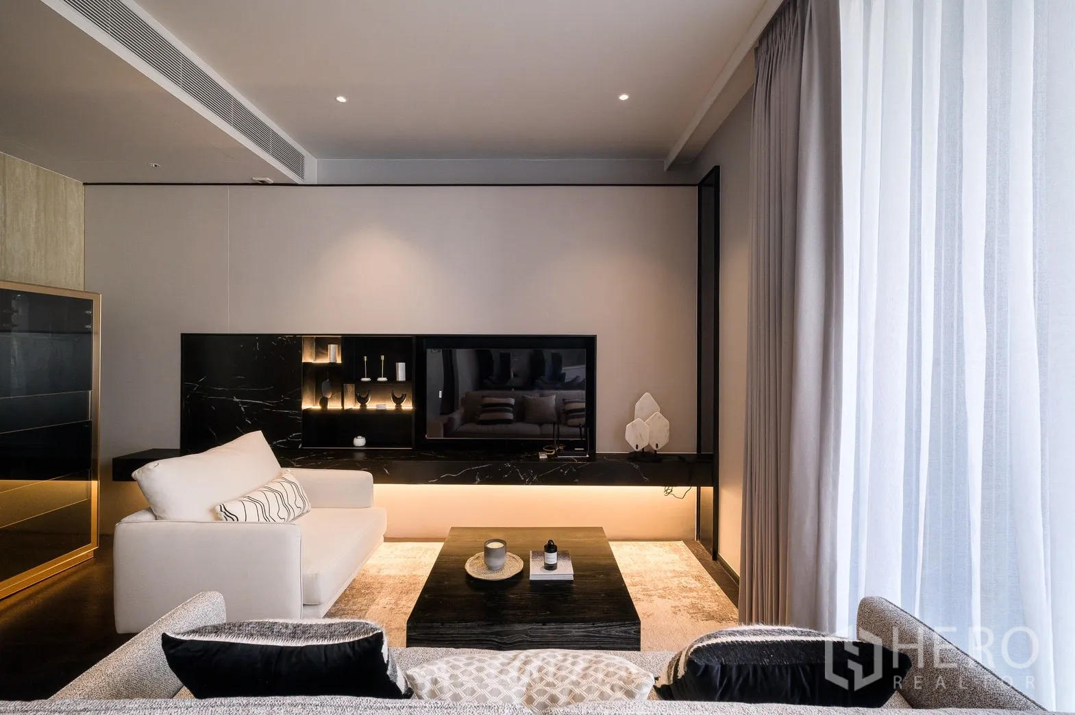 Condominium for rent or sale in Watthana, Bangkok - Contemporary lounge with marble TV wall, built-in shelving, soft lighting and two sofas around a low table.