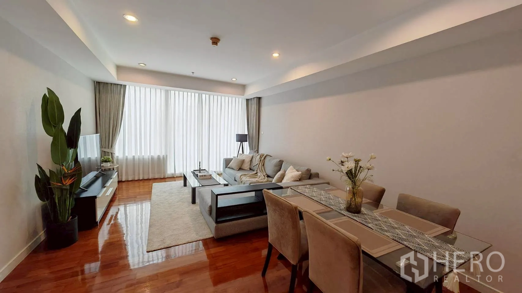 公寓 for rent in Khlong Toei, Bangkok - 客餐厅一体，设沙发、电视与餐桌，窗前纱帘采光。