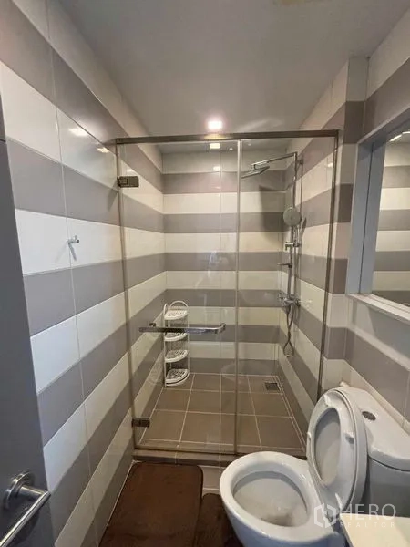 Condominium for rent or sale in Watthana, Bangkok - Striped-tile bathroom close-up showing glass shower with rain head and toilet.