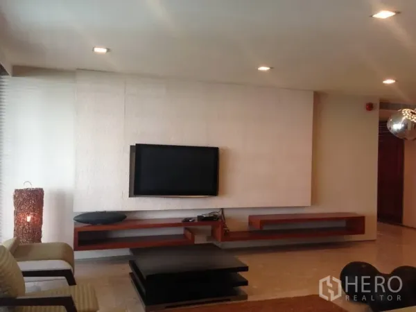 Condominium for rent or sale in Khlong Toei, Bangkok - Modern living room with wall-mounted TV, floating wooden shelves and recessed lighting in a Bangkok condominium.