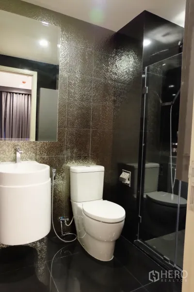Condominium for rent in Khlong Toei, Bangkok - Stylish bathroom with mosaic tiles, round vanity sink, toilet and glass shower enclosure.