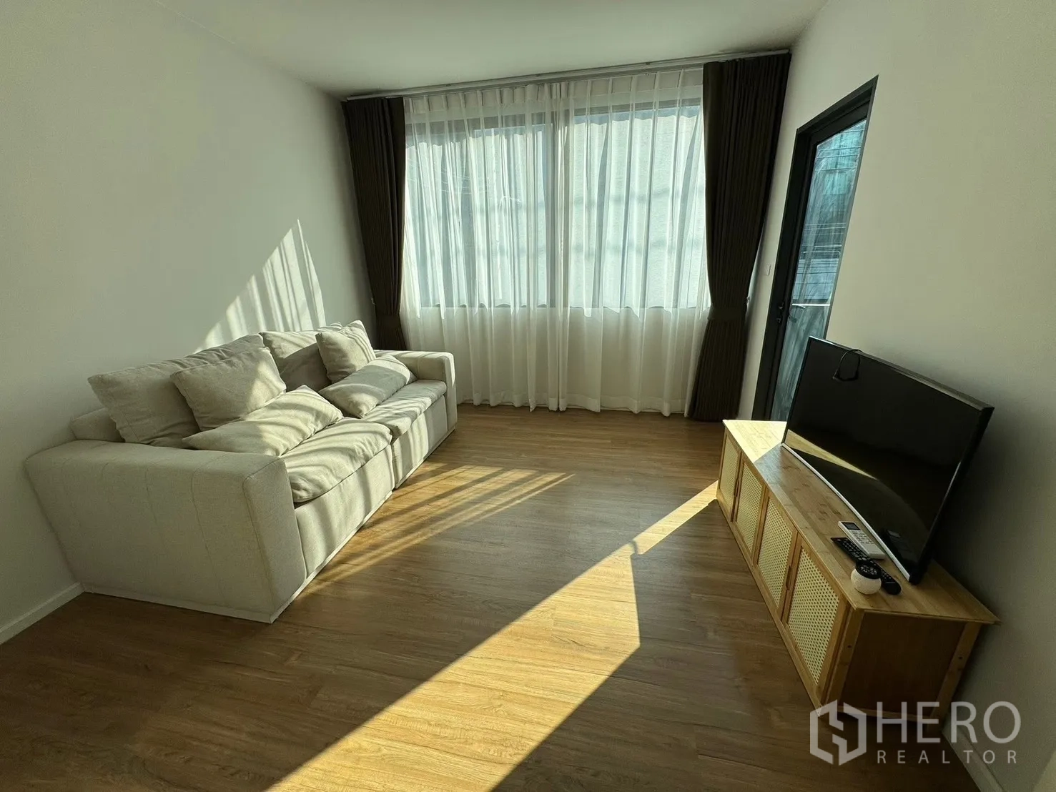 Townhouse for rent in Saphan Sung, Bangkok - Living room with sofa, TV console and full-length curtains.