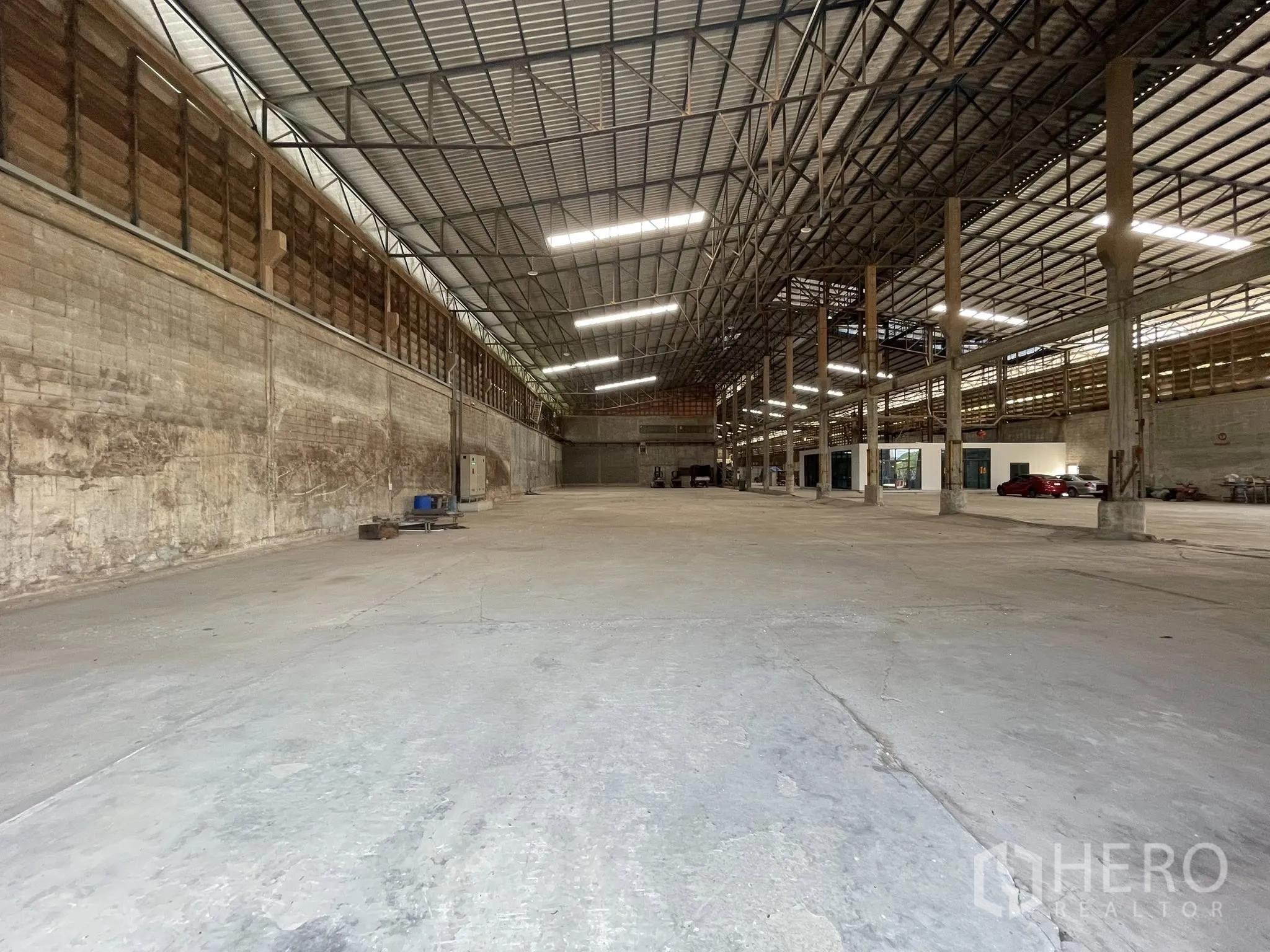 Factory for rent in Bang Bua Thong, Nonthaburi - Expansive warehouse interior with high steel truss roof, concrete floor, and small office rooms.