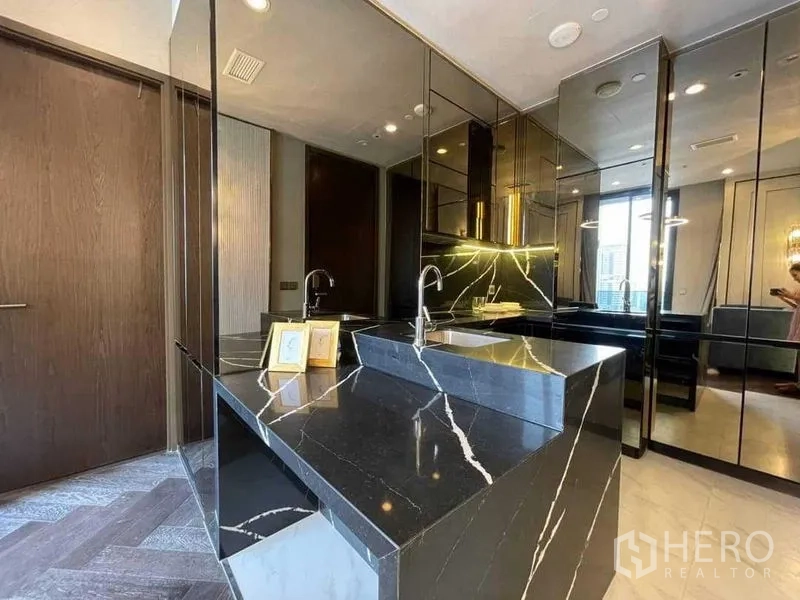 Condominium for rent in Khlong Toei, Bangkok - Polished black marble kitchen island with waterfall edge and reflective cabinetry.