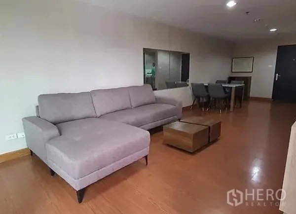 公寓 出租在Huai Khwang, Bangkok - 宽敞客厅，灰色L形沙发、木地板、茶几与用餐区。