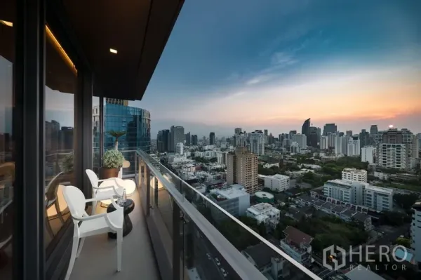 公寓 出售在Watthana, Bangkok - 高层阳台配座椅与玻璃栏杆，俯瞰城市日落景观。