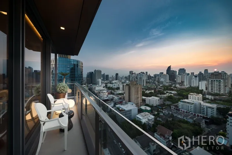 公寓 出售在Watthana, Bangkok - 高层阳台配座椅与玻璃栏杆，俯瞰城市日落景观。