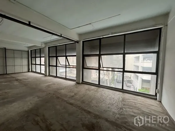 Retail Space for rent - Open-plan shop unit with large black-framed windows, concrete floor and industrial ceiling lighting overlooking the street.