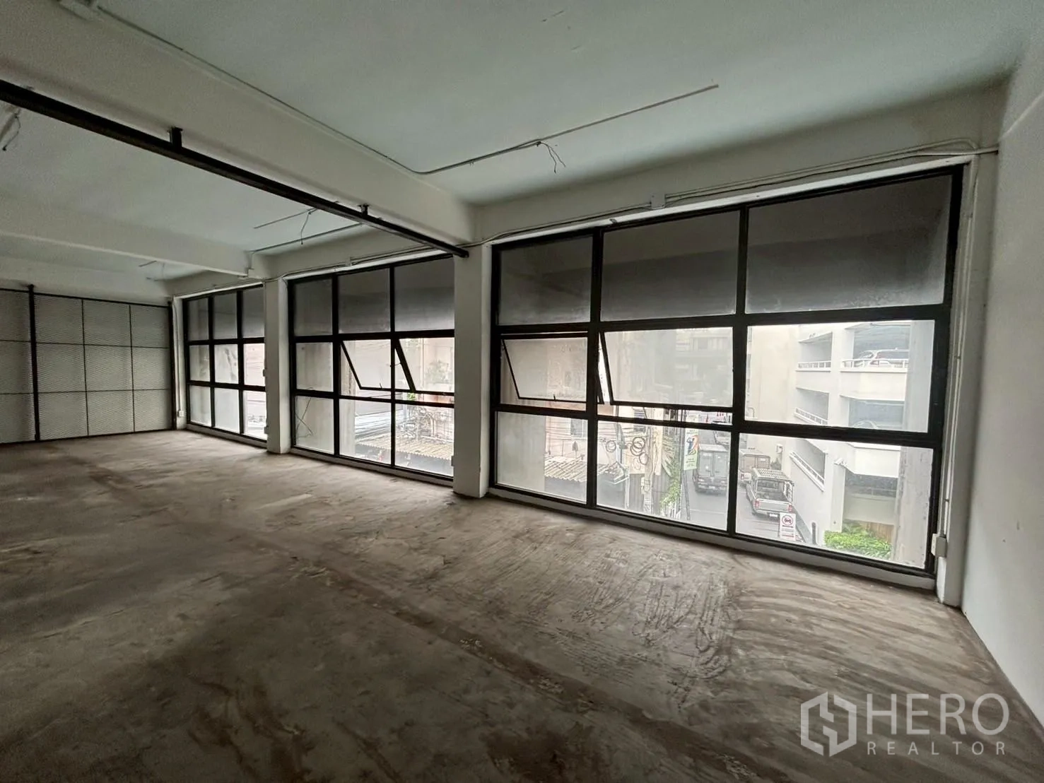 Retail Space for rent - Open-plan shop unit with large black-framed windows, concrete floor and industrial ceiling lighting overlooking the street.
