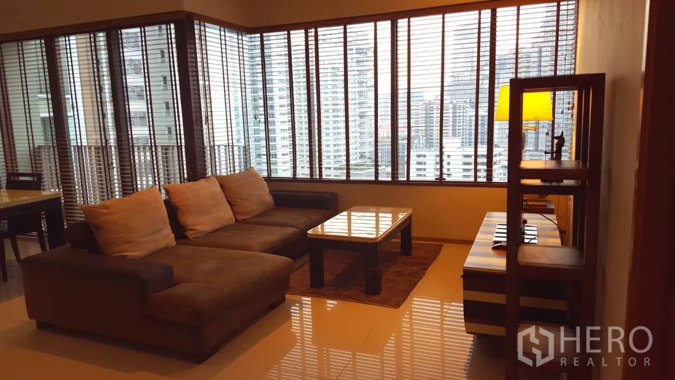 Condominium for rent or sale in Khlong Toei, Bangkok - Living room with sectional sofa, coffee table and wide city-view windows.