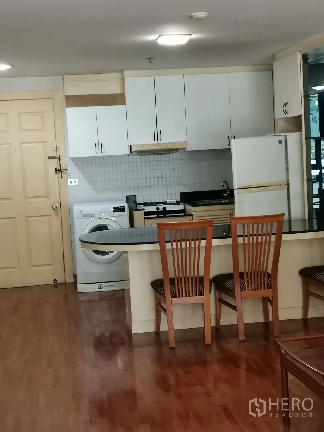 公寓 出租在Pathum Wan, Bangkok - 紧凑厨房配白色橱柜、吧台、冰箱与室内洗衣机，木地板。