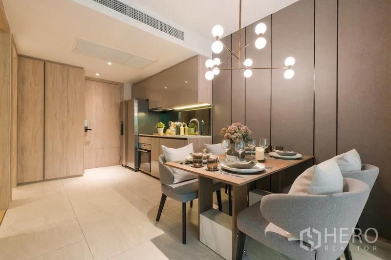 Condominium for rent in Watthana, Bangkok - Modern dining area with four-seat table, pendant chandelier, and a compact built-in kitchen.