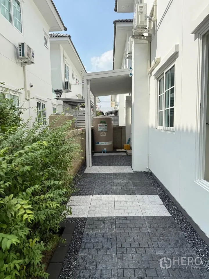 Semi-detached House for rent in Mueang Samut Prakan, Samut Prakan - Paved side yard with patterned tiles, hedges, and a covered utility area.