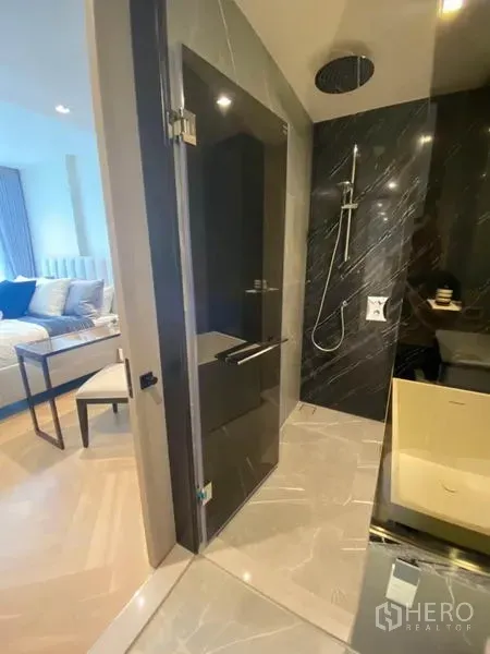 公寓 出租在Watthana, Bangkok - 酒店风格浴室，玻璃淋浴间、黑色大理石墙与顶喷花洒，后方可见卧室。