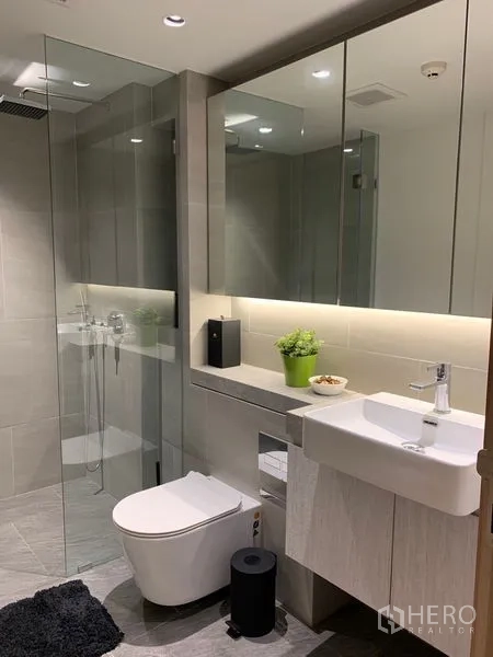 Condominium for rent in Bang Rak, Bangkok - Modern bathroom with glass-enclosed shower, large mirrored cabinets and vanity.