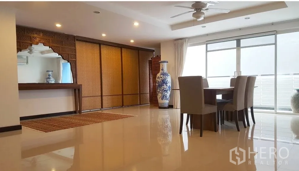 公寓 出租在Watthana, Bangkok - 曼谷瓦塔那区公寓的明亮客餐厅，落地推拉门通向阳台，天花风扇与雕花木饰。