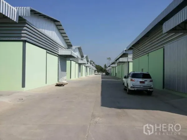 货栈 出租在Lam Luk Ka, Pathum Thani - 成排浅绿色仓库配金属屋顶，宽阔混凝土通道适合卡车通行。