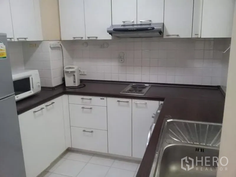 Condominium for rent in Watthana, Bangkok - U-shaped kitchen with white cabinets, cooktop, microwave and sink.