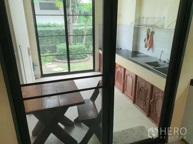 独立式住宅 出租在Mueang Nonthaburi, Nonthaburi - 半户外泰式厨房，水槽与灶台，滑门连接花园与木质餐桌。