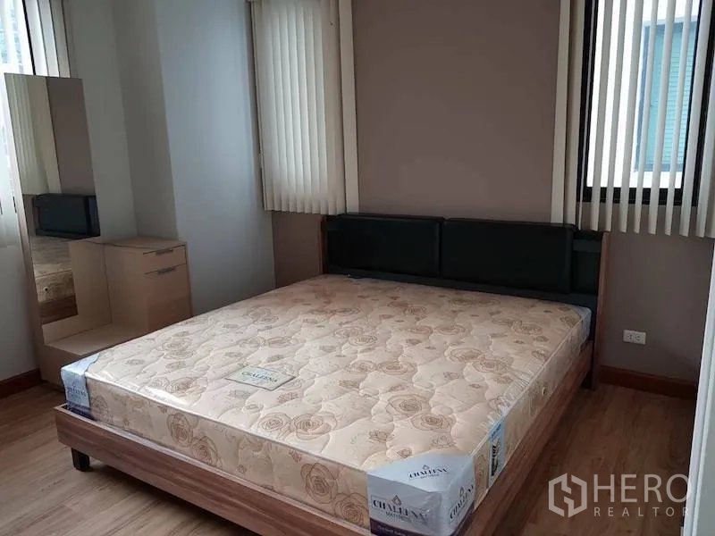 Condominium for rent in Watthana, Bangkok - Primary bedroom with large bed, corner windows with vertical blinds, and a dressing table with mirror.