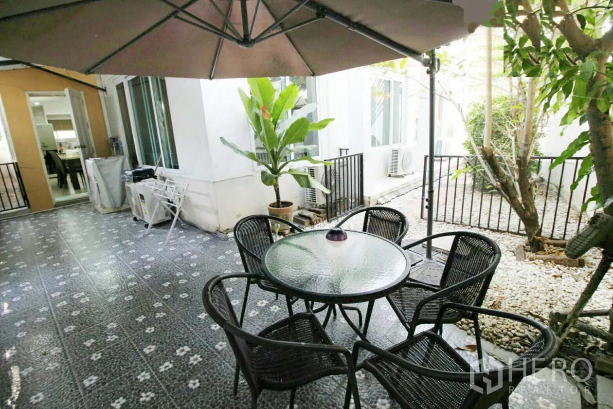Detached House for rent or sale in Lat Krabang, Bangkok - Shaded patio with round glass table, four wicker chairs and potted plants.