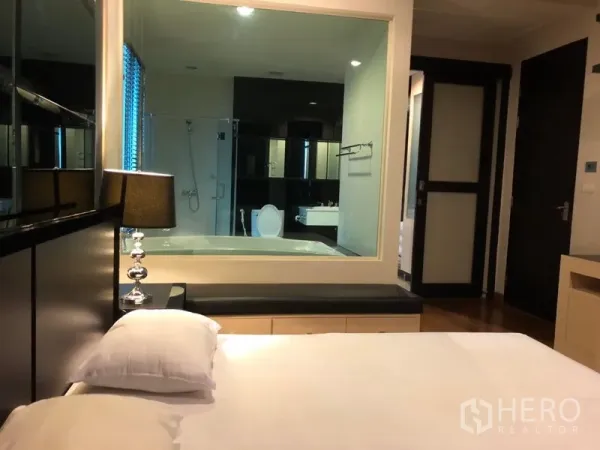 公寓 出租在Pathum Wan, Bangkok - 主卧带床头灯，透过玻璃可见带浴缸与淋浴间的套内卫浴。