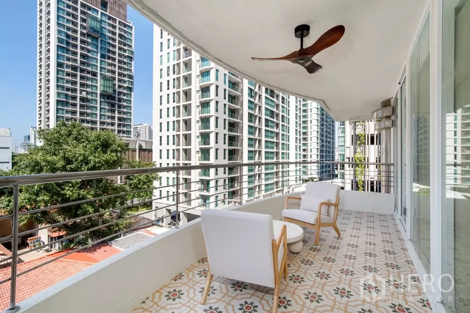Condominium for sale in Watthana, Bangkok - Phrom Phong condo balcony with lounge chairs overlooking Bangkok skyline and greenery.