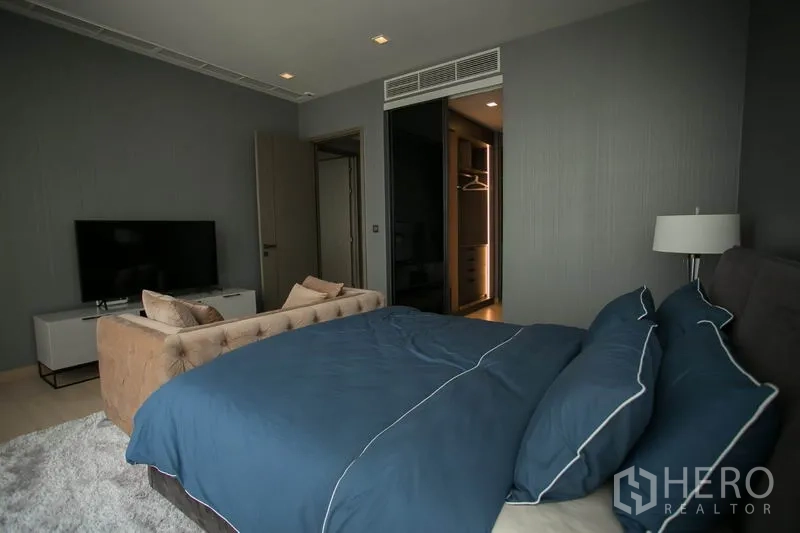 公寓 出租或出售在Watthana, Bangkok - 次卧蓝色床品，搭配电视柜与步入式衣帽间入口。