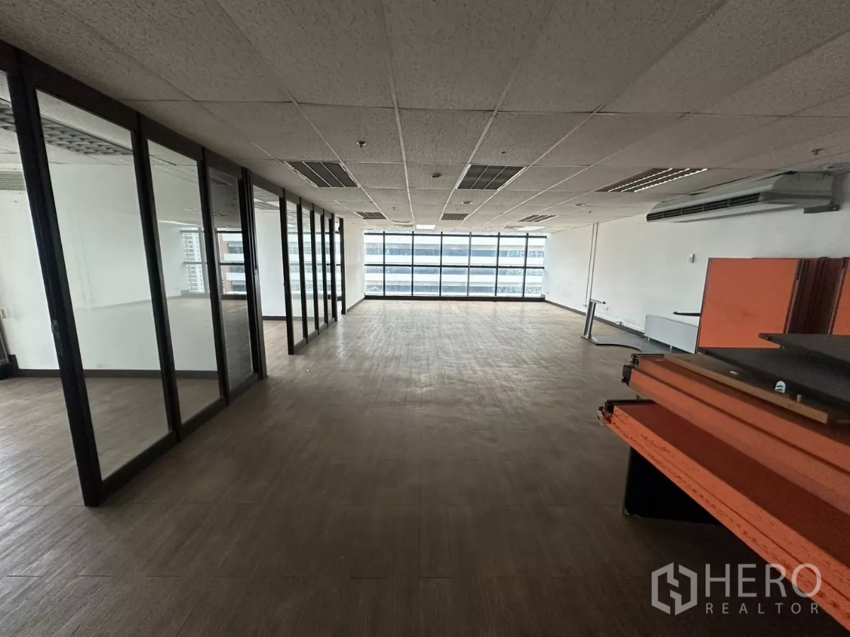 办公空间 出租在Watthana, Bangkok - 纵深办公带，左侧为整排玻璃隔断，尽头为大窗，通铺木纹地板。