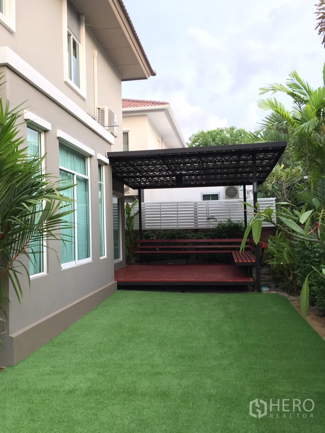 独立式住宅 出租在Pathum Thani - 后院铺人造草坪，带顶木质露台，邻屋侧。